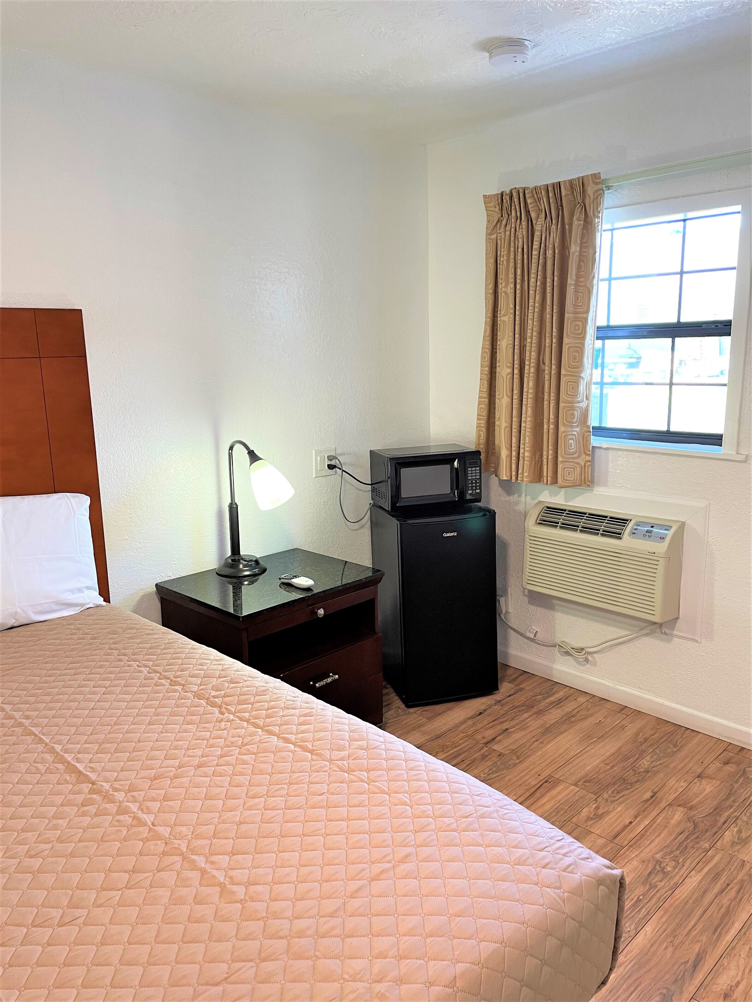 Una habitación de hotel con una cama, un escritorio con lámpara, microondas y aire acondicionado.