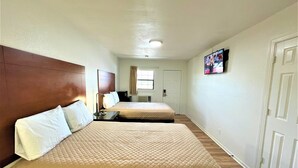 Habitación de hotel con dos camas, un televisor en la pared y una puerta al fondo.