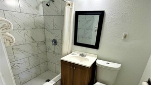 Un baño con ducha, inodoro, lavabo y espejo.