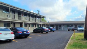 Un estacionamiento con varios autos, un motel con múltiples habitaciones y un cielo despejado.
