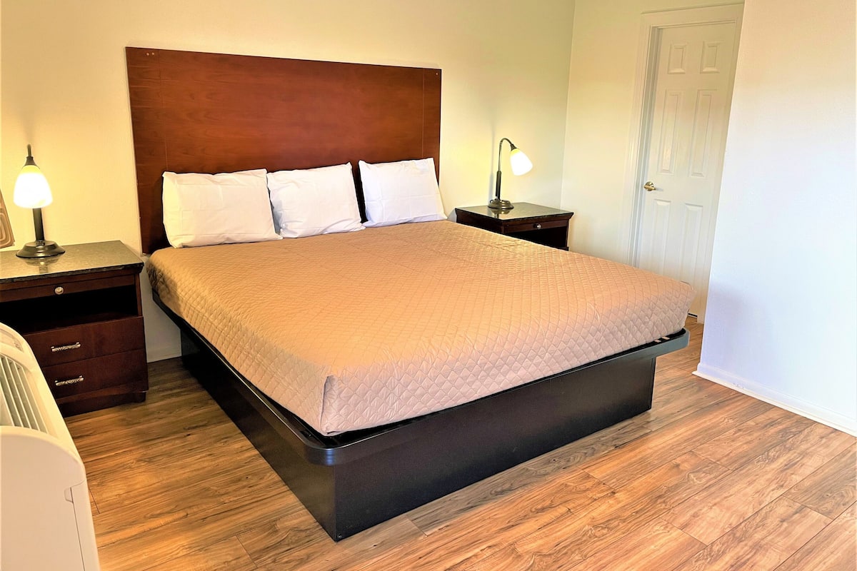 Una cama bien hecha con cabecera, dos mesitas de noche con lámparas y suelo de madera.