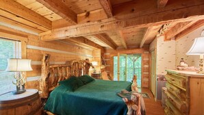 A rustic wooden room with a bed, wooden walls, and a large window. - “The Creel” Luxury 2BR Cabin with loft & view (Townsend)
