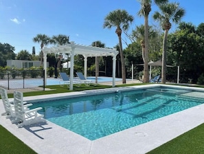 A rectangular swimming pool with clear blue water, surrounded by a white deck and a white pergola with a basketball hoop. - Containing Luxury in Jensen Beach-Starfish (Jensen Beach)