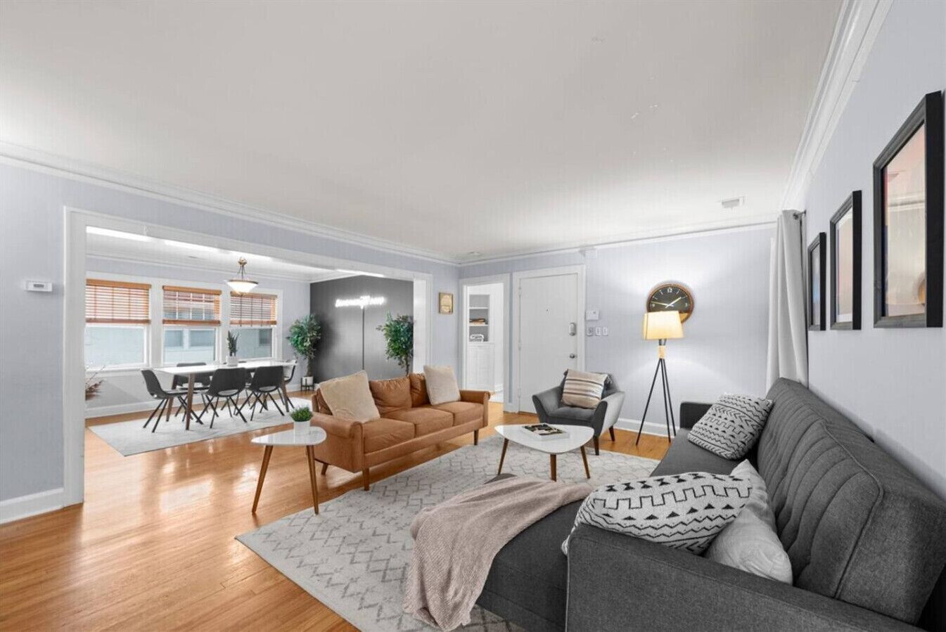 Un salon moderne avec un canapé gris, un canapé marron, un coin repas comprenant une table et des chaises, et un lampadaire.