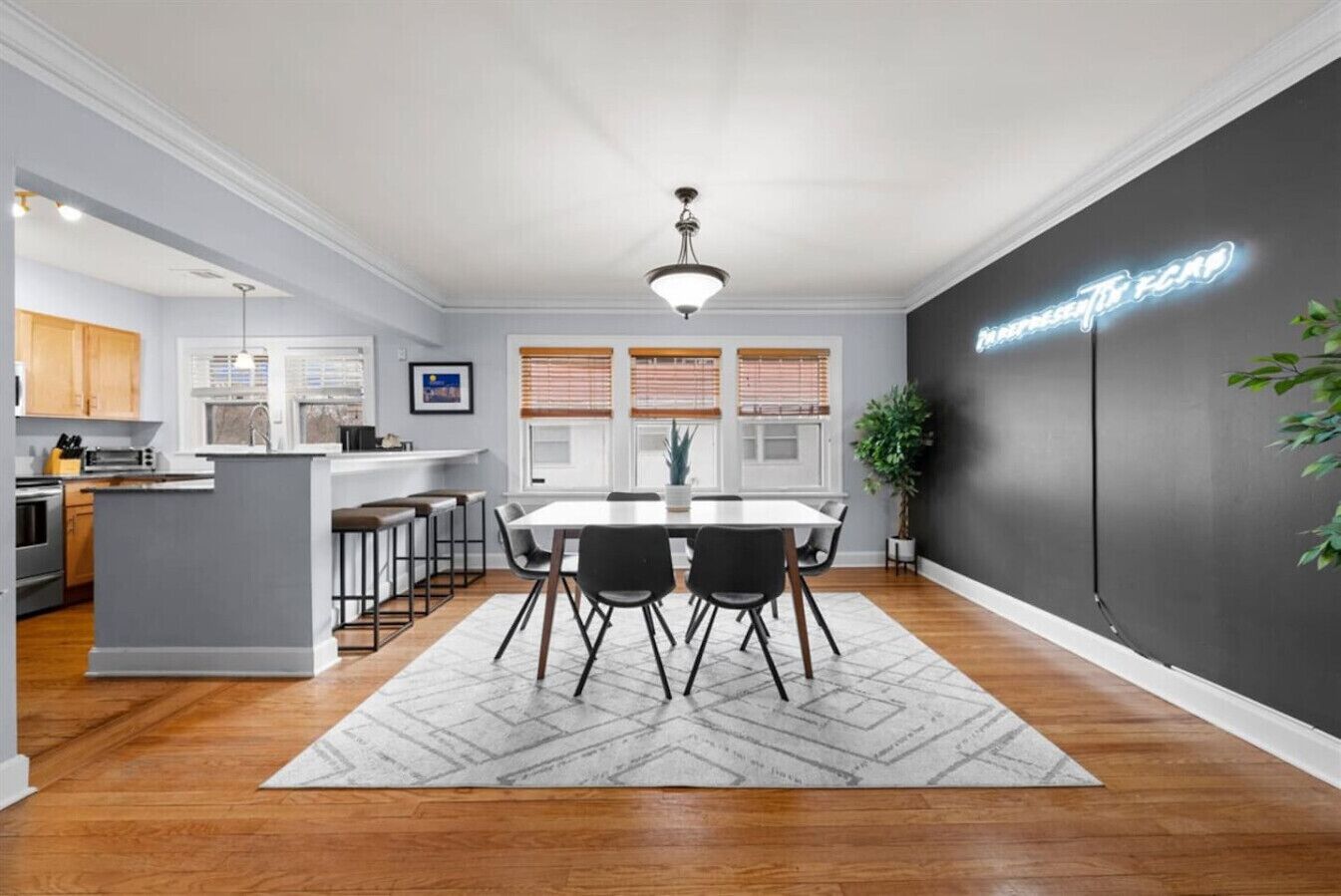 Une cuisine moderne dotée d’un îlot central, d’un coin repas avec une table blanche et des chaises noires, et d’un mur d’accent noir orné d’un néon.
