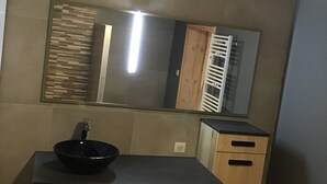 Un baño con tocador de madera, un lavabo negro y un espejo encima.