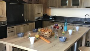 Una cocina con una isla grande, armarios de madera, una campana extractora negra y focos colgantes.