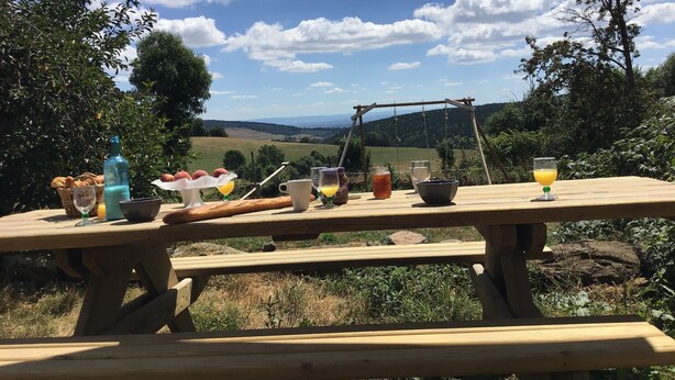 Una mesa de picnic de madera con vistas a un paisaje campestre, que incluye colinas ondulantes y un cielo despejado.