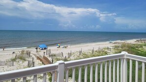 A beach view from a balcony with a wooden railing, sandy beach, and a clear sky. - Oceanfront family-sized beach house (Cape San Blas)