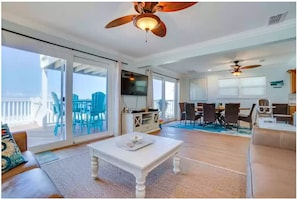 Relax in this stylish living area with a high ceiling, ceiling fan, and sliding glass door leading to an outdoor deck.