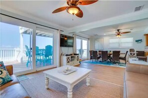 Relax in this stylish living area with a high ceiling, ceiling fan, and sliding glass door leading to an outdoor deck.