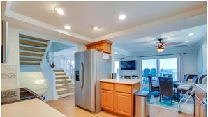 A modern kitchen with wooden cabinets, a built-in refrigerator, and a dining area with a table and chairs. - Oceanfront family-sized beach house (Cape San Blas)