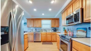 A modern kitchen with wooden cabinets, stainless steel appliances, and a central island. - Oceanfront family-sized beach house (Cape San Blas)