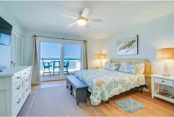 A bedroom with a bed, bedside tables, a ceiling fan, a window with a view, and a balcony with chairs.
