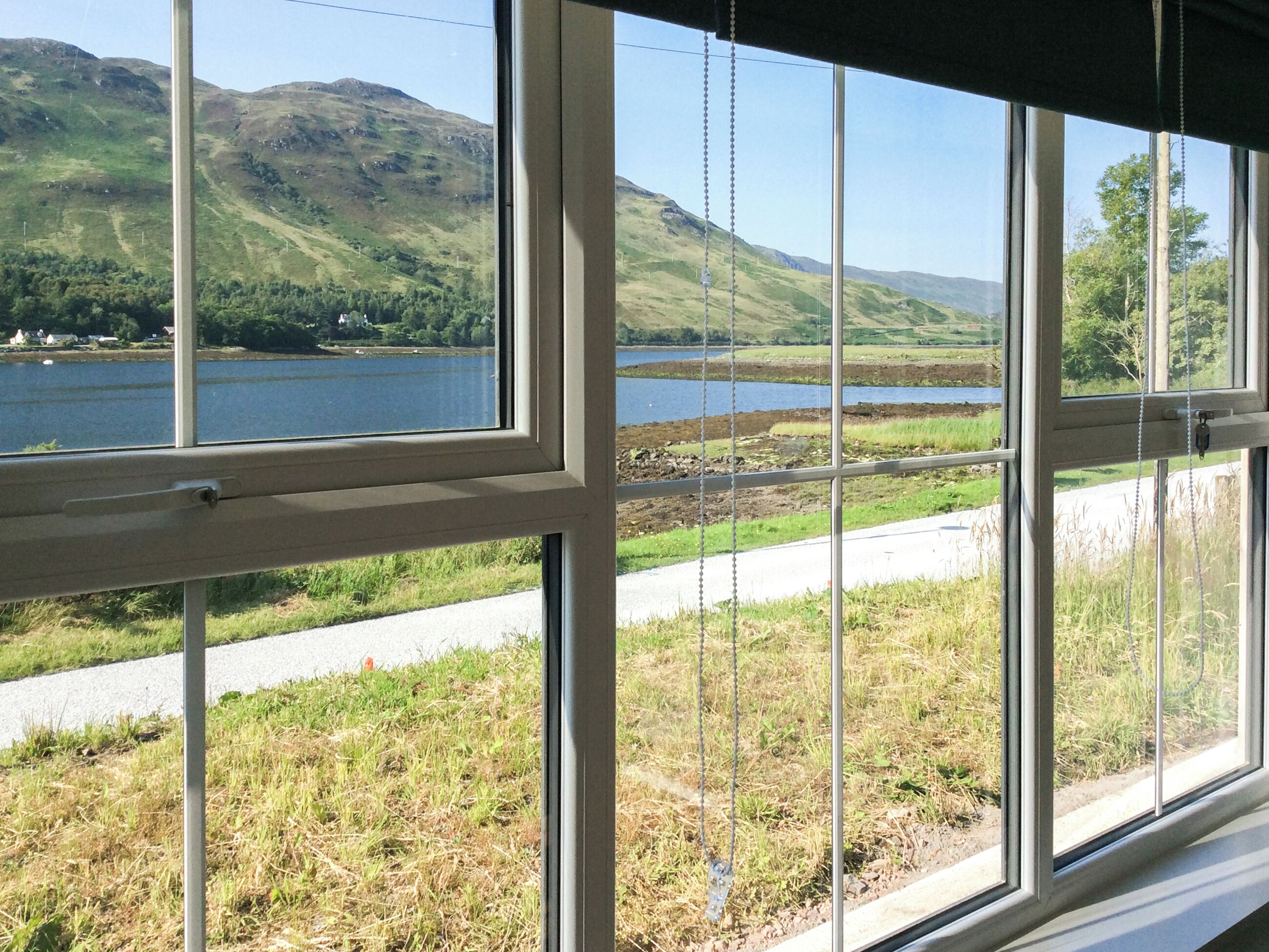 A window with a view of a lake, grassy areas, and hills.