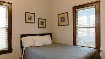 A bedroom with a bed, two windows, and three framed pictures on the wall.