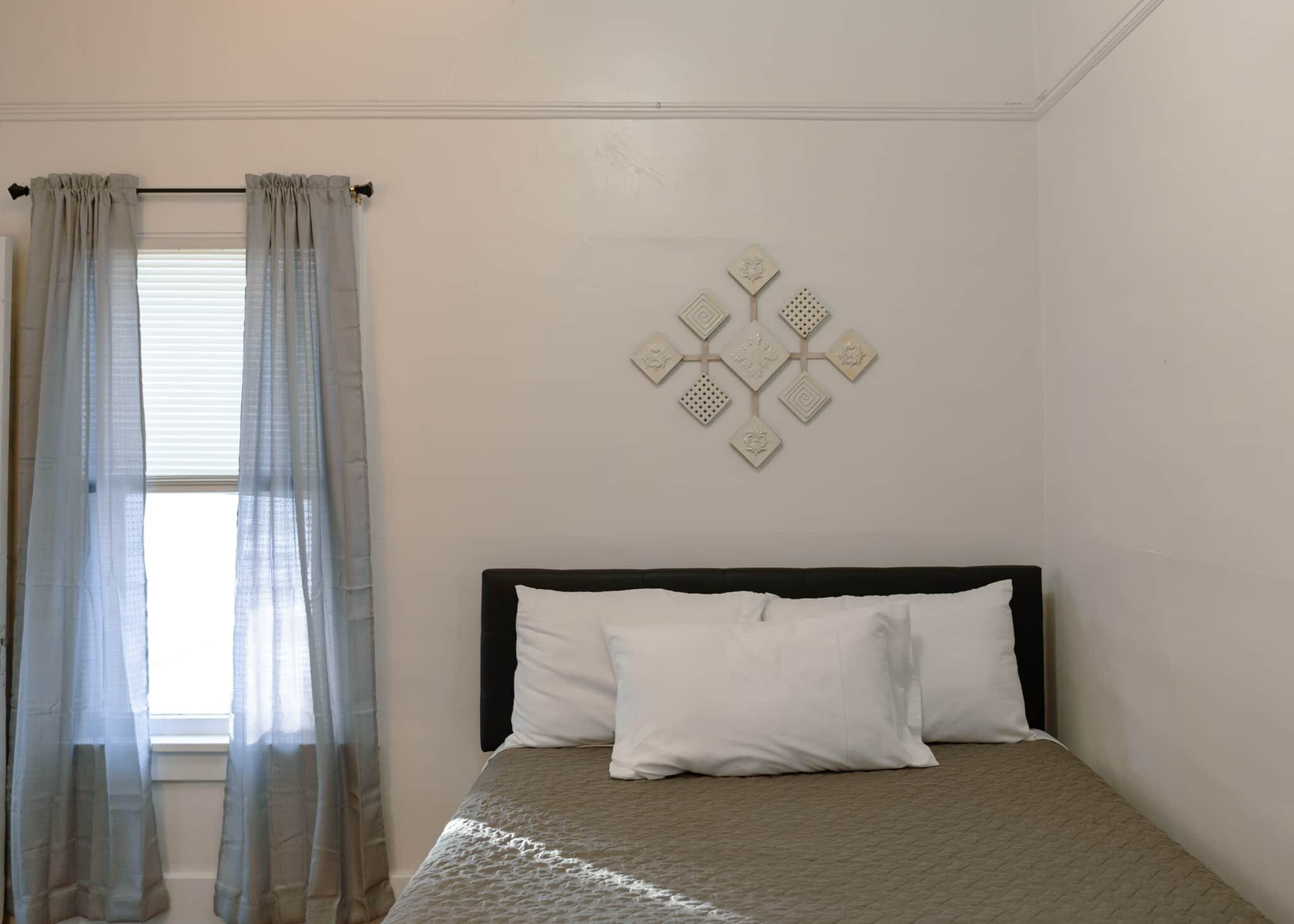 A bedroom with a bed, curtains, and a wall decoration.