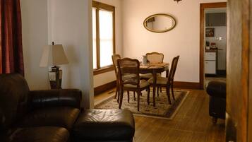 A living room with a brown leather sofa, a dining table with four chairs, a lamp, and a mirror on the wall.