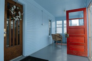 A hallway with a wooden door, a red door, and a wicker chair. - Red Roof Cottage – 2BR Mobridge Stay (Mobridge)