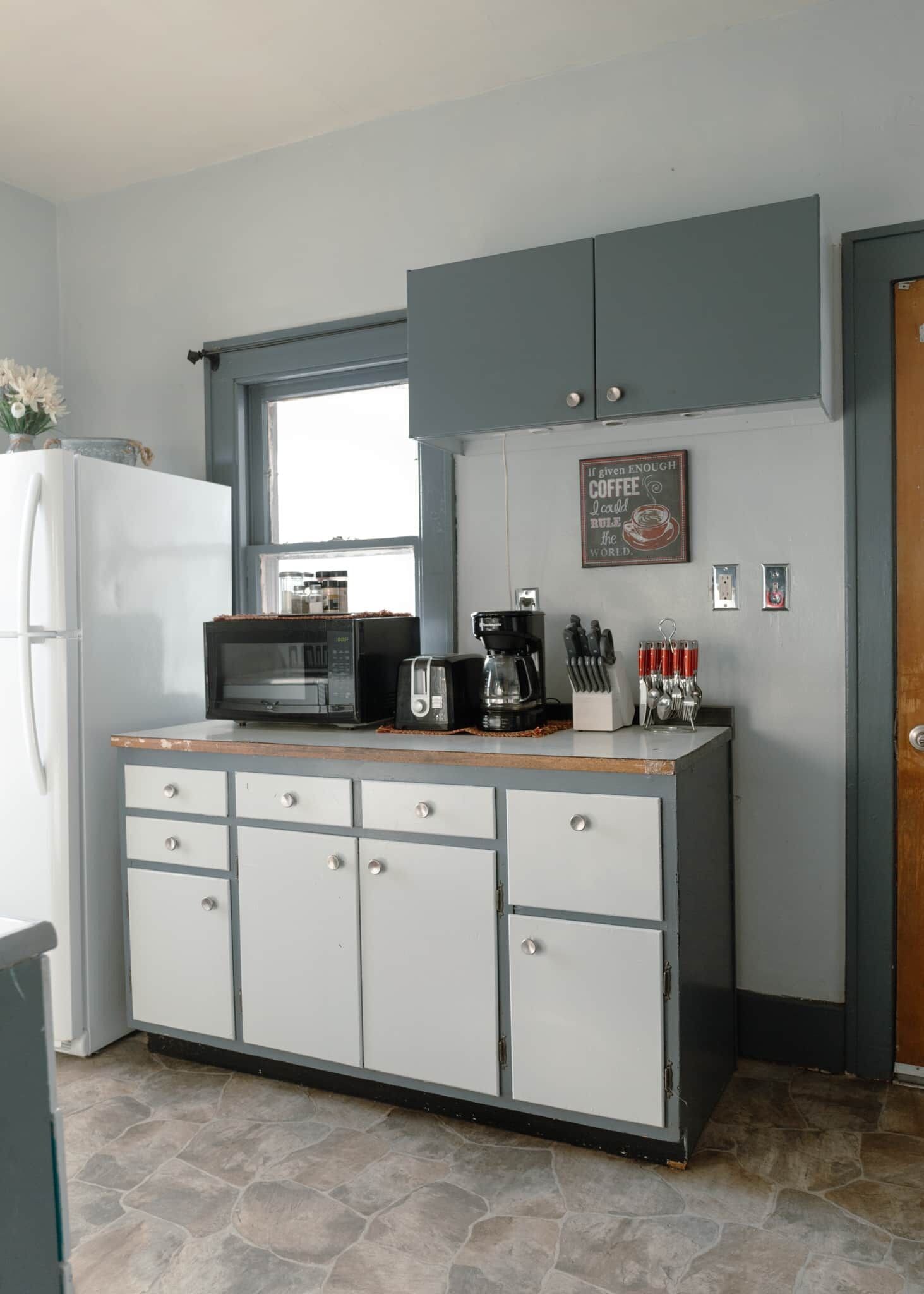 A kitchen with a refrigerator, microwave, coffee maker, and cabinets.