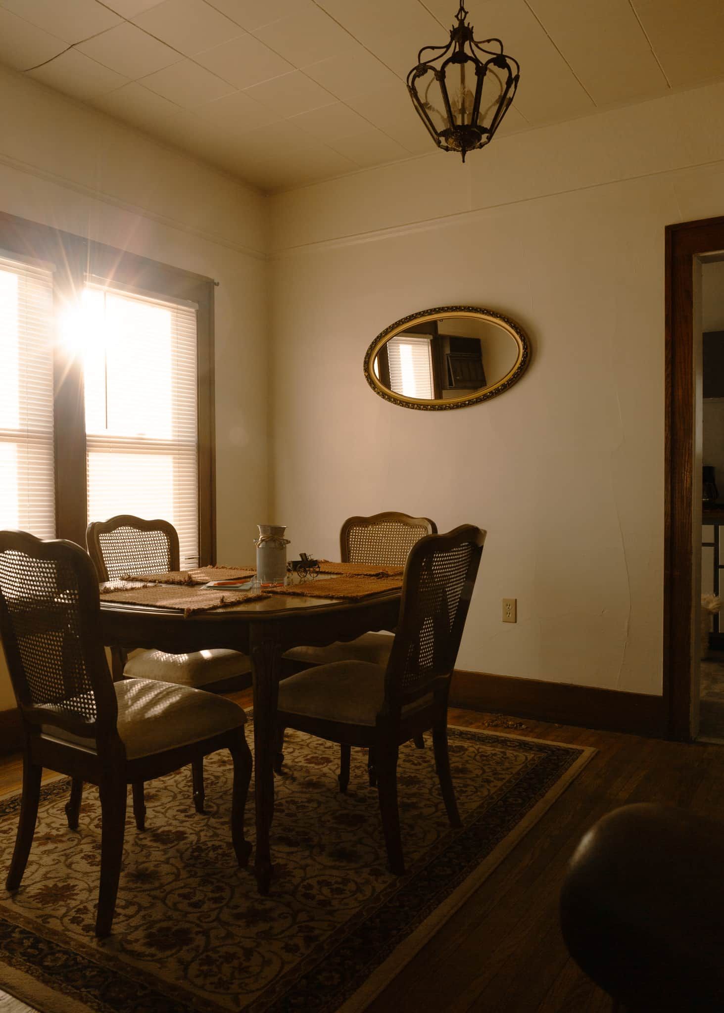 A dining room with a table, chairs, a chandelier, and a mirror on the wall.
