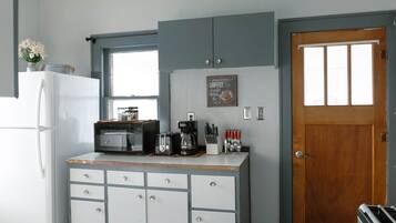 A compact kitchen with a refrigerator, microwave, toaster, coffee maker, and a wooden door.