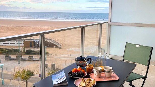 Un balcón con mesa dispuesto para el desayuno y vista a una playa.