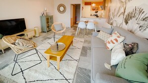 Una sala de estar con sofá, sillones, una mesa de centro, televisor, una zona de comedor y una cocina visible a través de una puerta abierta.