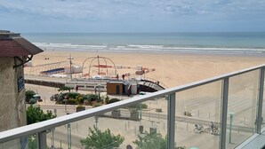 Vista a la playa desde un balcón, cielo despejado, arena y algunas personas a lo lejos.