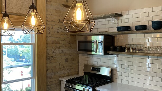 A modern kitchen with a gas stove, built-in oven, white cabinets, and a large window overlooking a street. - Moments to Fiserv Forum and Downtown Milwaukee! (Milwaukee)