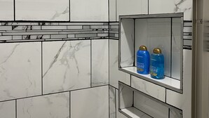 A bathroom with marble tiles, a built-in shelf with two bottles of shampoo, and a mirror. - Moments to Fiserv Forum and Downtown Milwaukee! (Milwaukee)