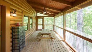 Eine Holzhütte mit überdachter Veranda, einer hölzernen Bank und einem Metallstauraum.