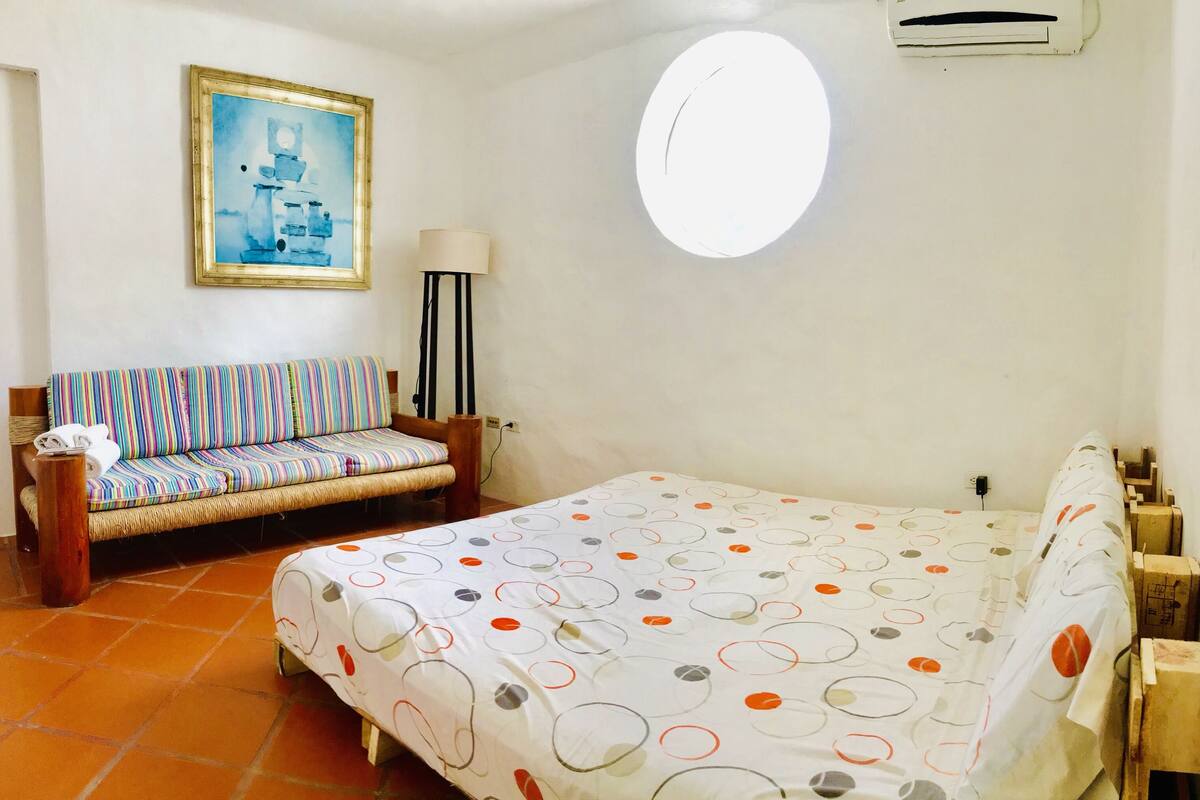 A bedroom with a bed, a sofa, a lamp, and a painting on the wall.