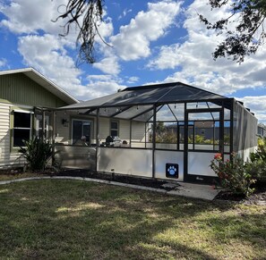 A house with a large glass-enclosed porch, a dog house with a paw print sticker, and a small garden area.