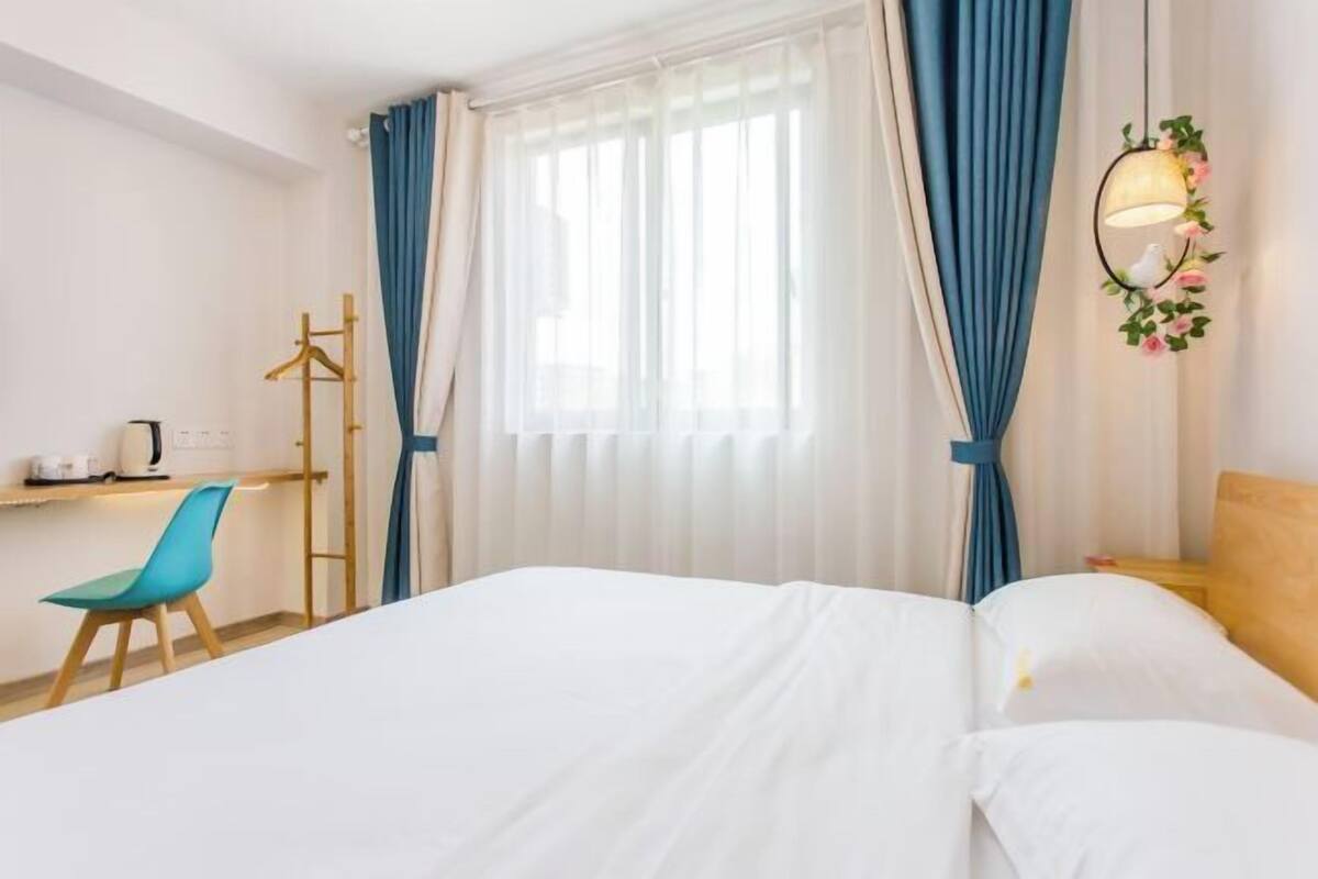 A hotel room with a bed, a desk with a chair, a wardrobe, and a window with curtains.