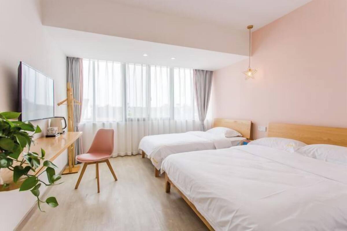 A hotel room with two beds, a desk, a chair, and a large window with curtains.
