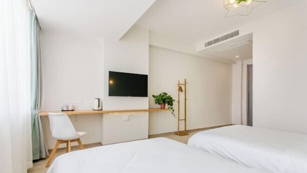 Quarto de hotel com cama, escrivaninha com cadeira, televisão e planta.