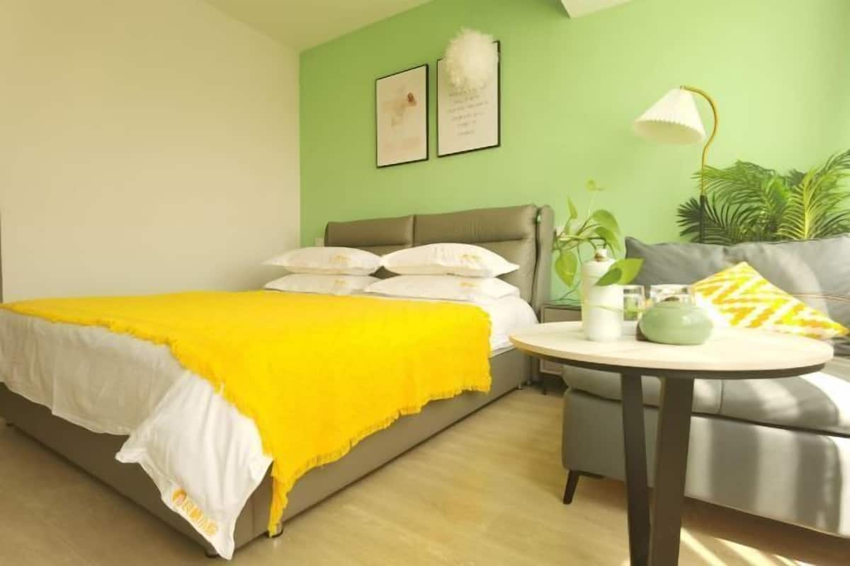 A bedroom with a bed, a round table, a sofa, and a green wall.