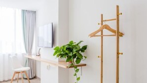 Quarto moderno com porta-roupas de madeira, TV na parede, cadeira branca e planta em vaso sobre uma prateleira.