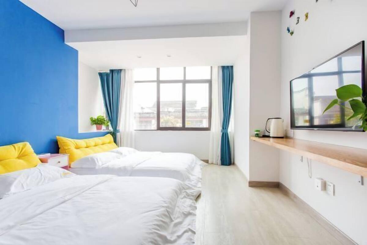 A hotel room with two beds, a large window, a TV, and a wooden shelf.