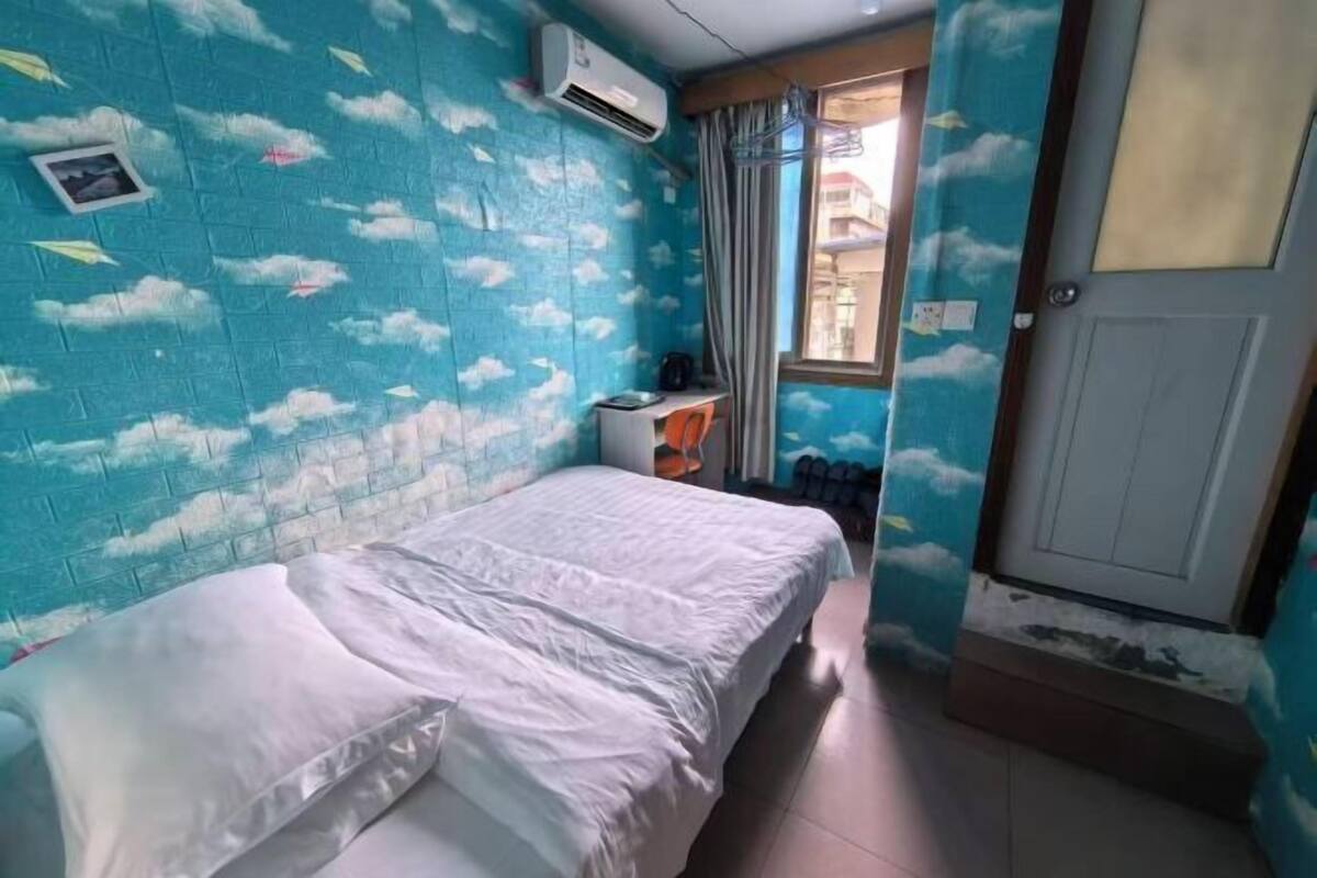A room with a bed, a window with curtains, a door, and an air conditioning unit.