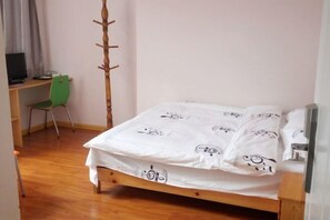 A bedroom with a wooden bed, a green chair, a desk with a computer, and a coat rack. - Huashuwanbinguan (Changsha)