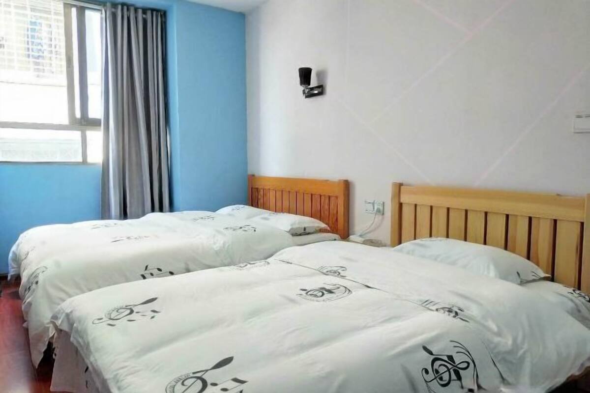 A room with two beds, a window with curtains, a wall-mounted light, and a wooden headboard.