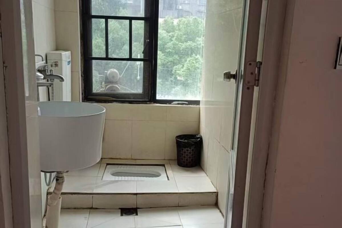 A small bathroom with a white sink, a window, and a black trash bin.