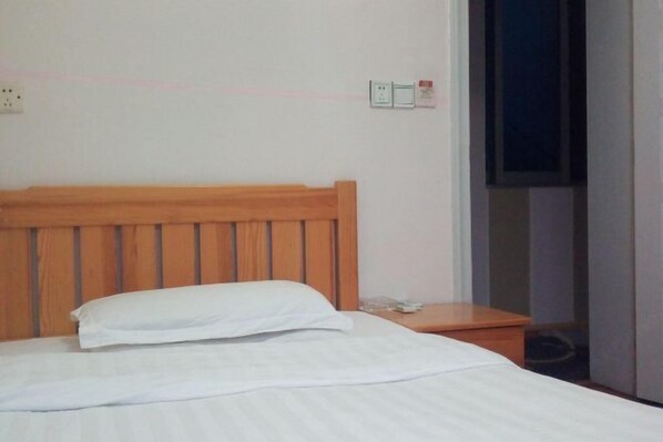 A neatly made bed with a wooden headboard in a hotel room. - Huashuwanbinguan (Changsha)