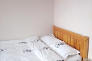 A single bed with a wooden headboard, white bedding with a pattern, and a small bedside table with a lamp. - Huashuwanbinguan (Changsha)