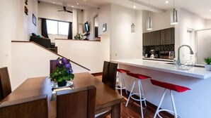 Cozinha moderna com bancada branca, banquetas vermelhas e área de refeições com mesa e cadeiras de madeira.