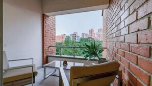 Varanda com parede de tijolos, mesa de vidro, duas cadeiras e um vaso com planta.
