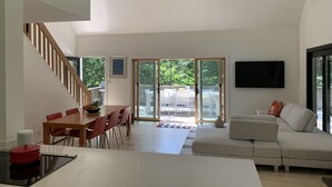 Een moderne woonkamer met een bank, een eettafel met stoelen, een keuken met een fornuis en een trap naar een verdieping erboven.