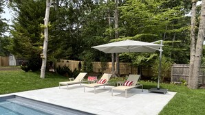 Een achtertuin met een zwembad, twee ligstoelen en een grote parasol.